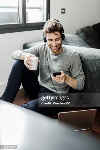 smiling young man with cell phone, laptop and headphones at home - premiere of vertical entertainments in darkness arrivals stockfoto's en -beelden