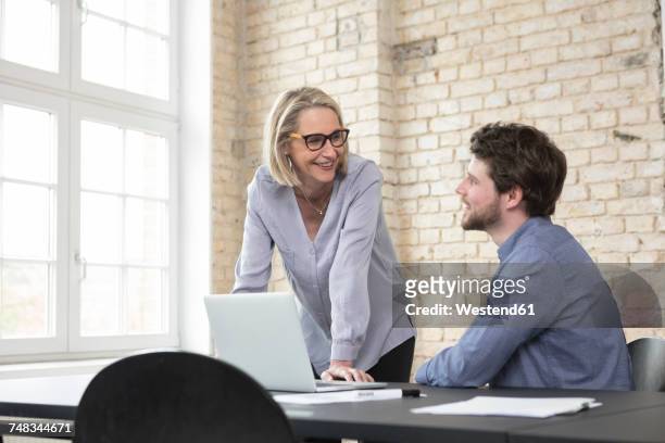 mature businesswoman working with younger colleague in office - older woman younger man stock-fotos und bilder