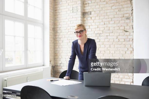 successful businesswoman standing in her office - pleased face laptop stock pictures, royalty-free photos & images