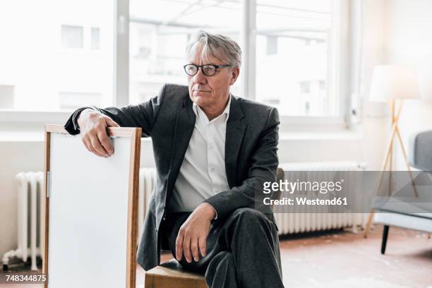 senior businessman sitting on chair with picture frame - sitting chair office relax stockfoto's en -beelden
