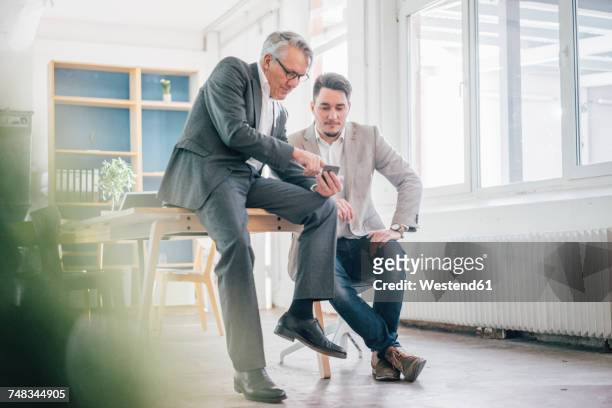 senior businessman showing cell phone to young businessman - father son business stock-fotos und bilder