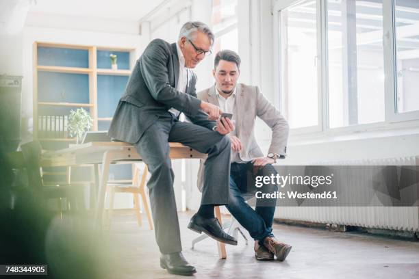 senior businessman showing cell phone to young businessman - família de duas gerações - fotografias e filmes do acervo