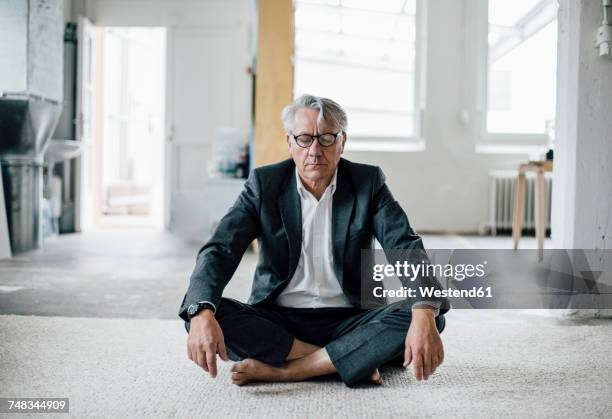 senior businessman sitting on floor meditating - senior yoga stock-fotos und bilder