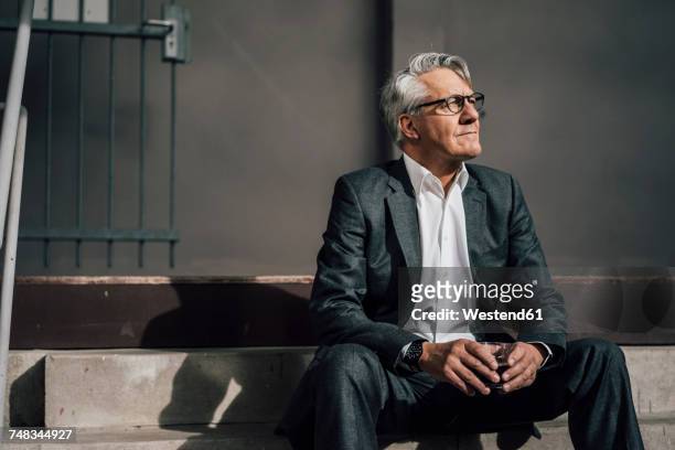 senior businessman sitting on concrete stairs - dreiviertelansicht stock-fotos und bilder