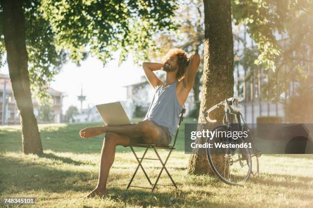 man with beard and curly hair using laptop in park - landleben stock-fotos und bilder