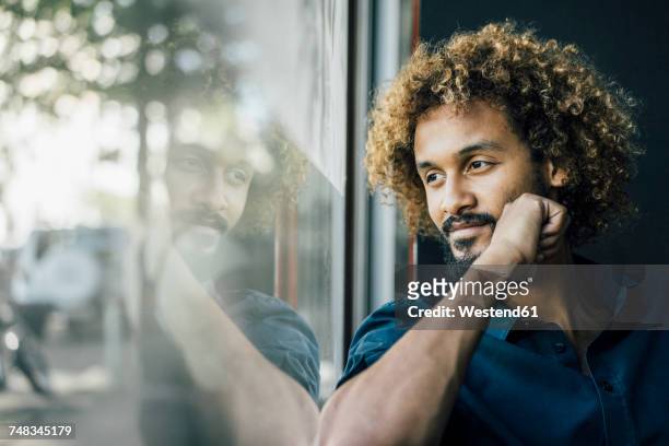 man with beard and curly hair looking out of window - reflection stock-fotos und bilder