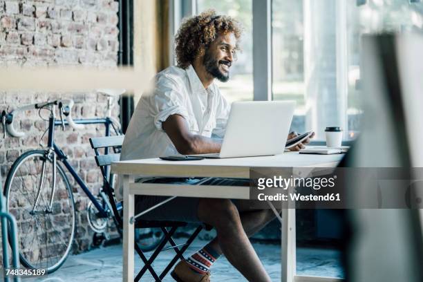 smiling young man at desk with laptop - men shorts stock pictures, royalty-free photos & images