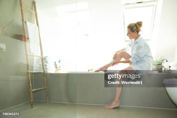 woman sitting on edge of bathtub creaming her leg - older woman legs fotografías e imágenes de stock