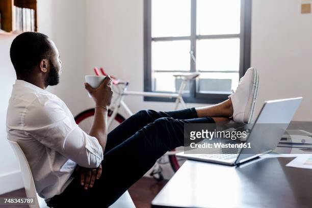 relaxed man in home office with feet on desk - businessman working on a laptop with a coffee stock-fotos und bilder