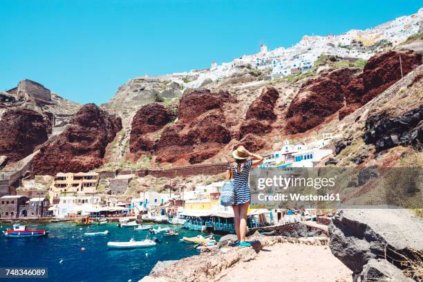 greece, santorini, oia, woman enjoying the view in the fishing harbor with the white village above the cliff - santorin stock pictures, royalty-free photos & images