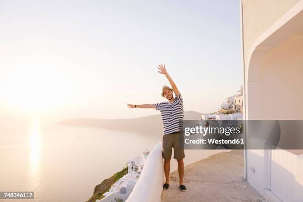 greece, santorini, fira, happy man on holidays with hands up enjoying the sunset over the sea - happy holidays around the world stock pictures, royalty-free photos & images