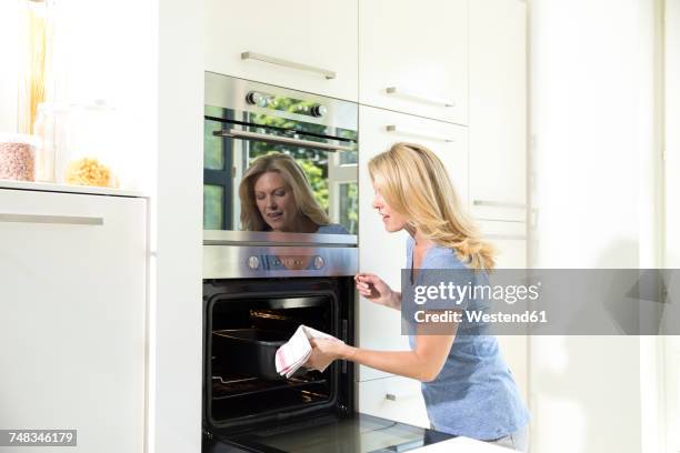 woman in kitchen taking casserole dish out of oven - hot wife stockfoto's en -beelden