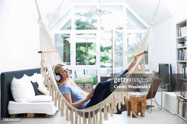 relaxed woman at home lying in hammock listening to music - frau kopfhörer indoor stock-fotos und bilder