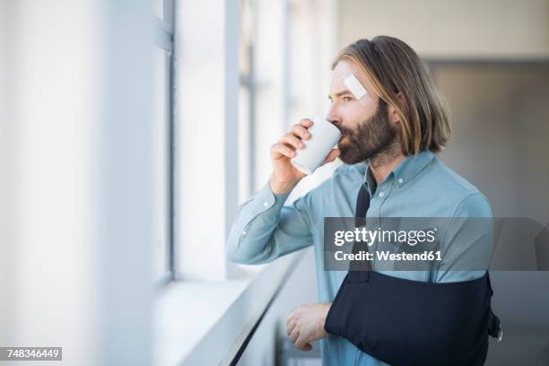 employee with sling drinking coffee by the window - cabestrillo-de-brazo fotografías e imágenes de stock