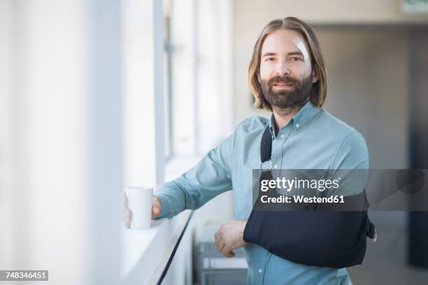 employee with sling standing by the window - cabestrillo de brazo fotografías e imágenes de stock