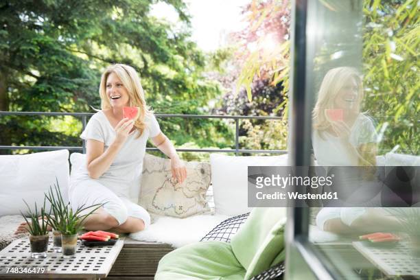 mature woman sitting on balcony, eating water melon - alleen één oudere vrouw stockfoto's en -beelden