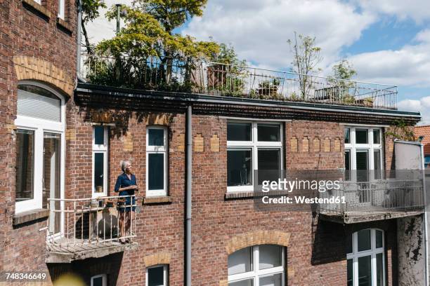 woman standing on balcony of brick house - coffee break outside stock pictures, royalty-free photos & images