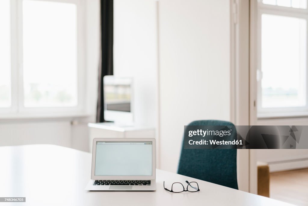 Laptop and glasses on table in office