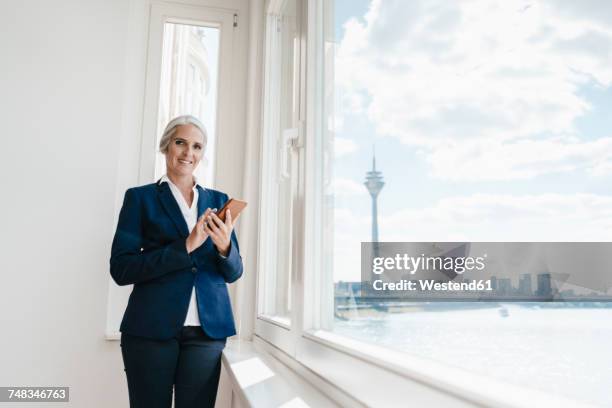 portrait of confident businesswoman holding cell phone in waterfront office - büro und wolke stock-fotos und bilder