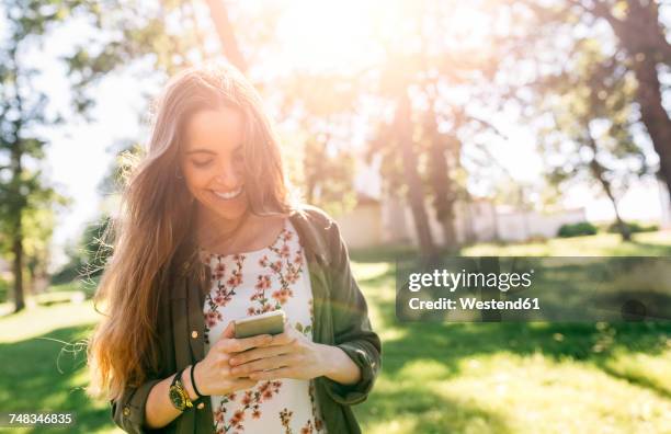 young woman sending messages with her smartphone - woman smartphone nature stockfoto's en -beelden