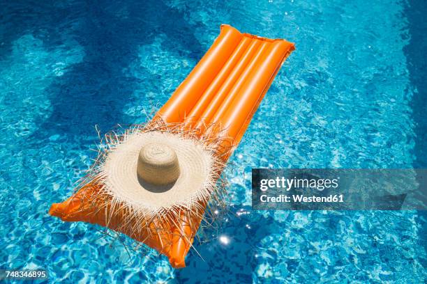 straw hat on orange airbed in swimming pool - luftmatratze von oben stock-fotos und bilder