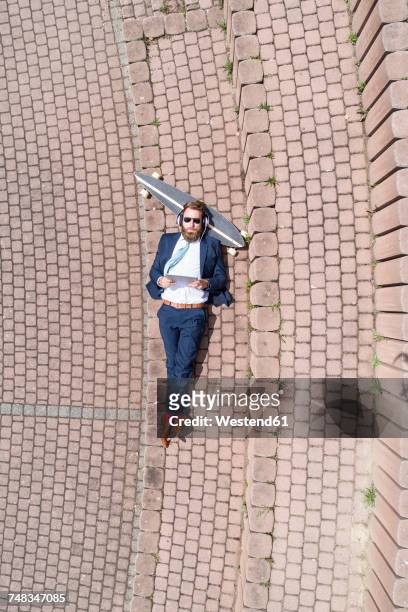 businessman with skateboard lying on a wall using tablet and headphones - business recovery stock pictures, royalty-free photos & images