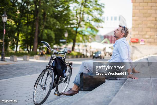 relaxed man sitting on stairs in the city next to bicycle - münchen business stock pictures, royalty-free photos & images