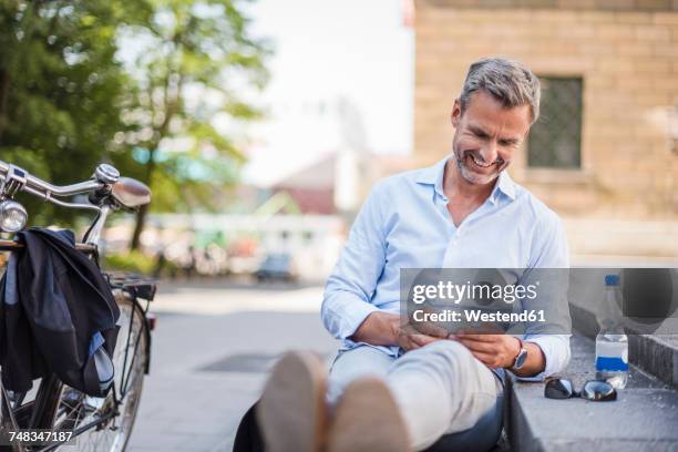 smiling man sitting on stairs in the city using cell phone - münchen business stock pictures, royalty-free photos & images