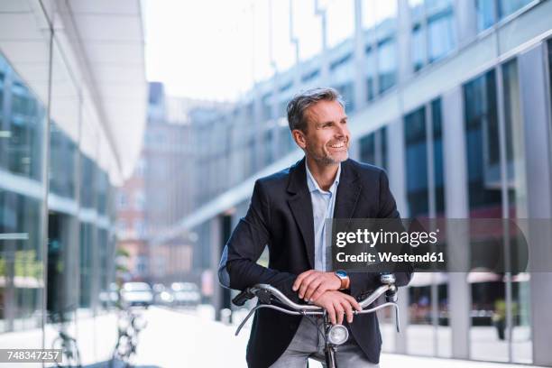 smiling businessman on bicycle in the city - munich business stock pictures, royalty-free photos & images