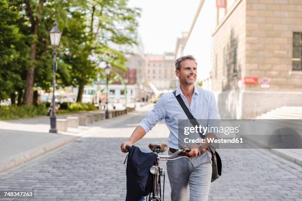 smiling man pushing bicycle in the city - bolsa de hombro fotografías e imágenes de stock