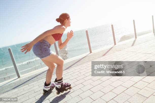 young woman inline skating on boardwalk at the coast - inline skating - fotografias e filmes do acervo