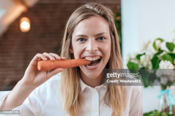 portrait of young woman biting carrot - zahn stock-fotos und bilder
