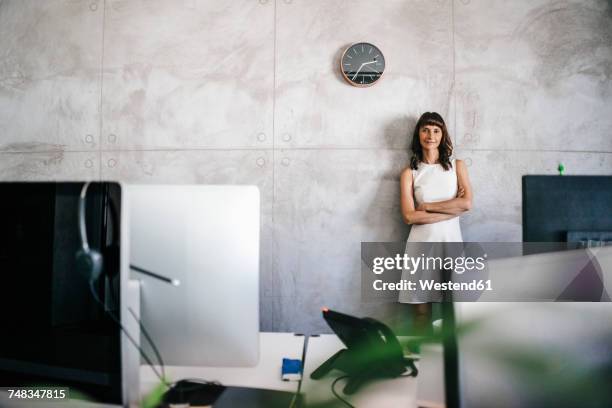 businesswoman standing under wall clock with arms crossed - businesswoman under stock-fotos und bilder