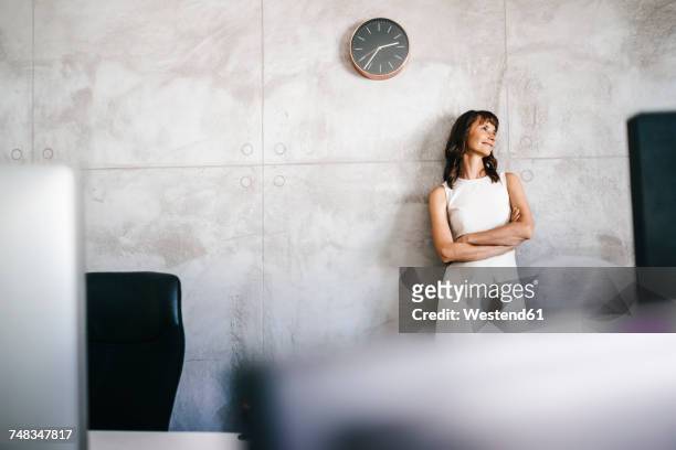 businesswoman standing under wall clock with arms crossed - clock on wall stock pictures, royalty-free photos & images