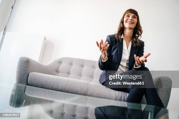 businesswoman sitting on couch, gesturing - formelle geschäftskleidung stock-fotos und bilder