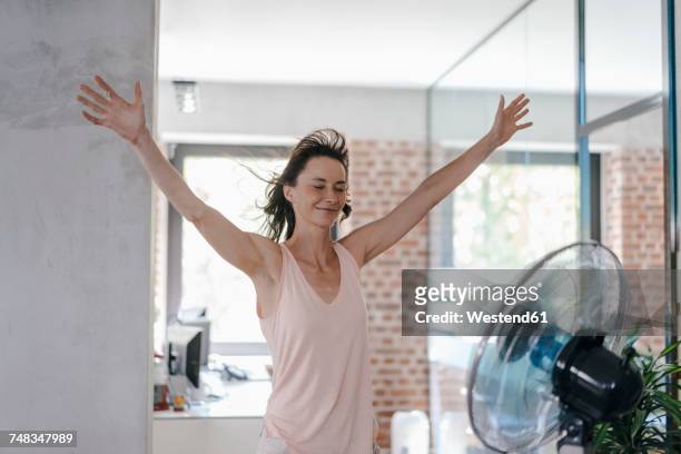 businesswoman in office enjoying breeze from a fan - warm stockfoto's en -beelden