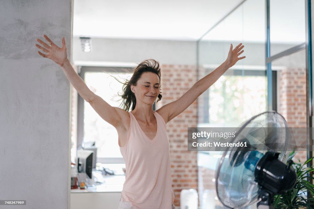 Businesswoman in office enjoying breeze from a fan