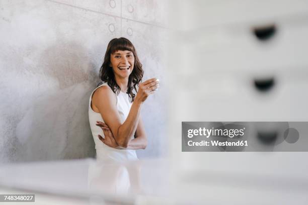 woman drinking coffee in office, leaning against wall - portrait im raum stock-fotos und bilder