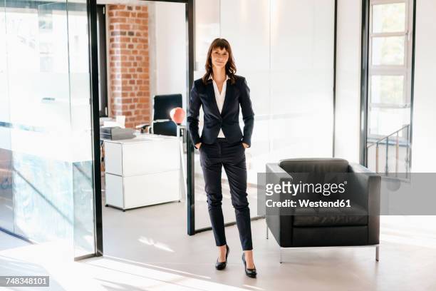 successful businesswoman standing in office with hands in pockets - geschäftskleidung stock-fotos und bilder