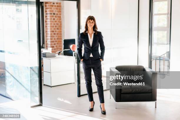 successful businesswoman standing in office with hands in pockets - tailleur pantalon photos et images de collection