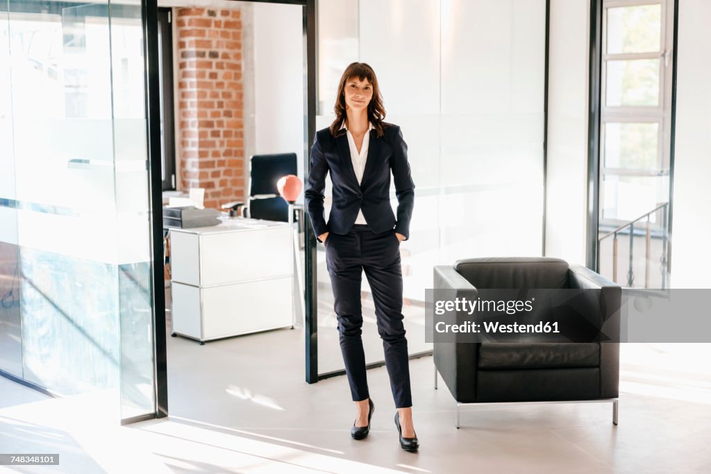 Successful businesswoman standing in office with hands in pockets