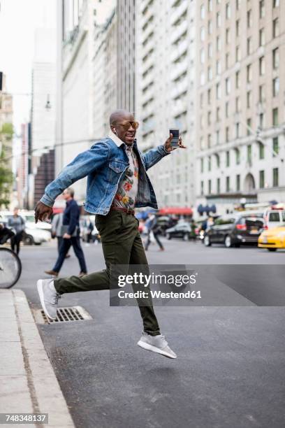 usa, new york city, manhattan, stylish man jumping in the air - young man listening to music on smart phone outdoors stockfoto's en -beelden