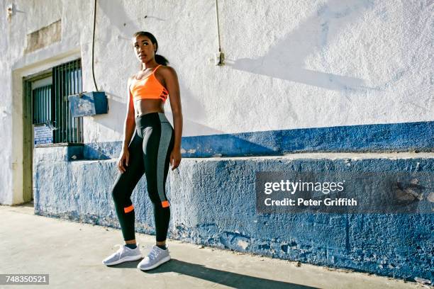 mixed race woman standing near urban wall - maillot de sport stockfoto's en -beelden