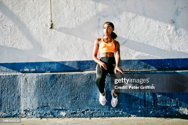 mixed race woman sitting on ledge of urban wall - sims stock-fotos und bilder