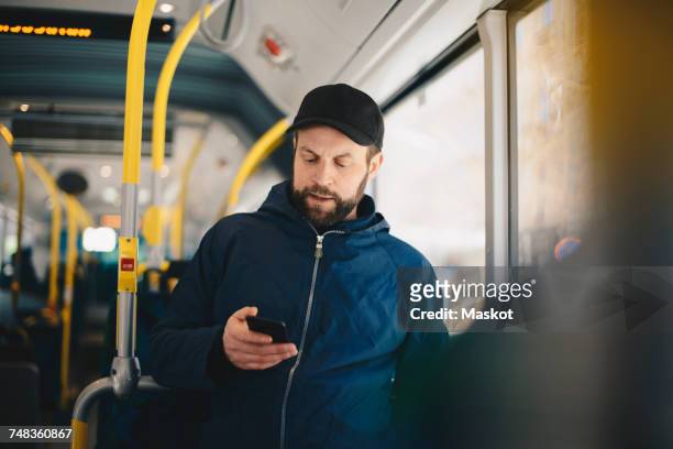male commuter using mobile phone while traveling in bus on sunny day - autobus foto e immagini stock