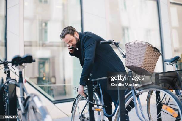 man talking on mobile phone while unlocking bicycle in city - stockholm park stock pictures, royalty-free photos & images