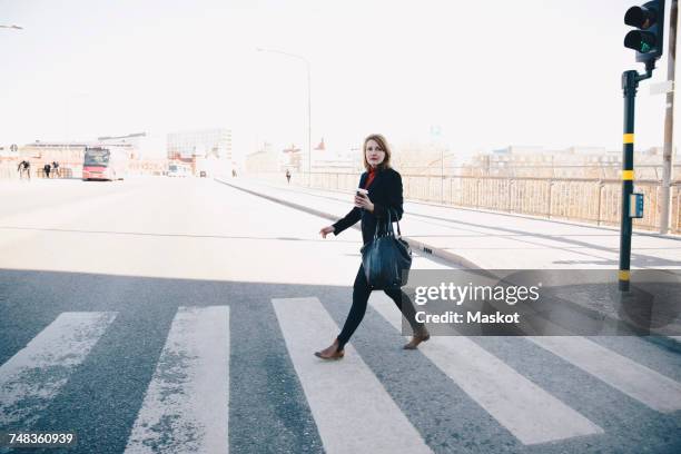 full length of woman with bag walking on zebra crossing in city against clear sky during sunny day - pavement cafe - fotografias e filmes do acervo