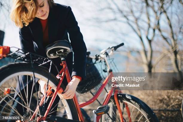 woman bending while locking bicycle on sunny day during winter - schloss abschließen stock-fotos und bilder