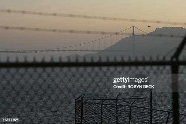 San Francisco, UNITED STATES: The Golden Gate Bridge is visible through the fence and barbed wire surrounding the prison recreation yard as the sun...