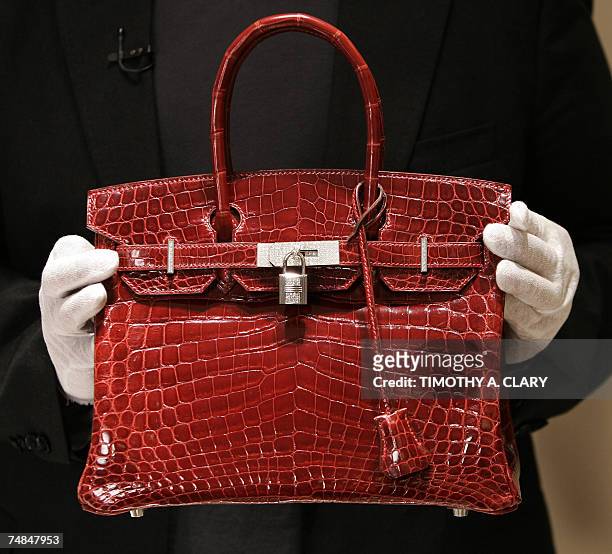 New York, UNITED STATES: A employee holds a 129,000 USD crocodile Hermes Birkin Bag for the press to see during a private opening for the new Hermes...